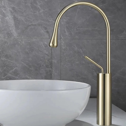 The Tiqui™ Single Handle Bathroom Sink Faucet in brushed gold, featuring a sleek curved high-arc spout, is elegantly mounted above a round white ceramic basin. Complementing the design is a matching shower head, set against a backdrop of gray marble-patterned tiles.