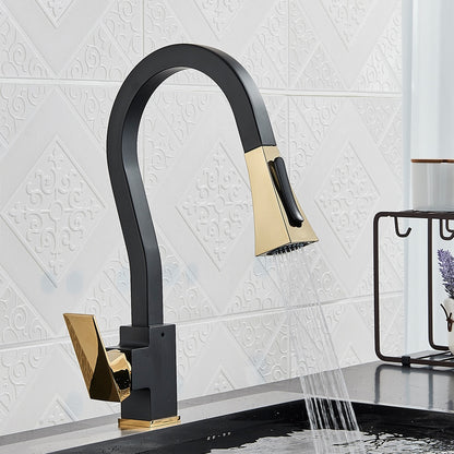 A modern kitchen features the Rozin Gourmet Kitchen Faucet with Flexible Pull Down Sprayer, elegantly designed in black and gold, set against a white textured tile backsplash. Water cascades from the faucet into a sleek dark countertop sink. In the background, a small wire shelf adorned with a lavender sprig and soap dispenser adds to the contemporary appeal of the space.