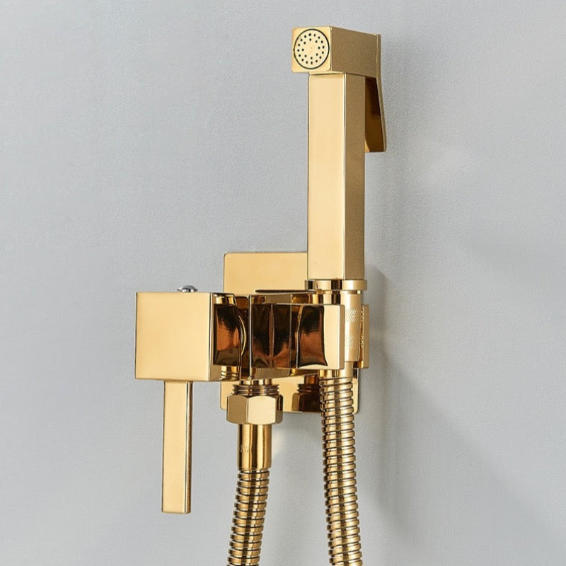 A Polished Gold Wall Mounted Toilet Sprayer Bidet Faucet by Morsale.com is elegantly captured on a light gray wall. The set features a handheld spray nozzle with a control lever and a flexible metal hose connected to a control valve unit, seamlessly complementing the nearby bathroom sink faucet for a cohesive look.