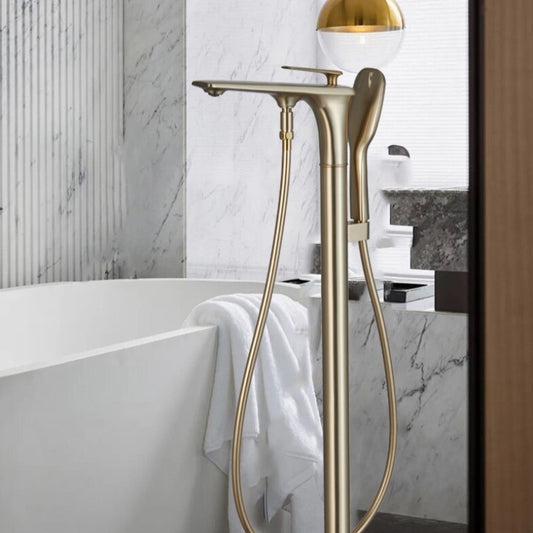 A modern bathroom featuring a freestanding bathtub complemented by a Mike Jake Brushed Gold Floor Mounted Bathtub Faucet Shower Mixer. The wall behind the tub is elegantly adorned with white marble, while a white towel drapes over the edge of the tub. To the right, a wooden door frame peeks into view.