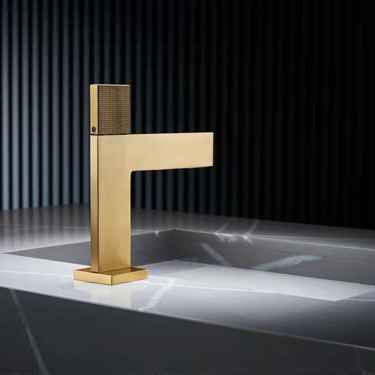 A sleek, modern Mike Jake Single Handle Brass Bathroom Sink Faucet in gold is pouring water into a gray sink. The sink, reminiscent of high-end bathroom fixtures, features a minimalist design with clean lines. The background shows vertical paneling, adding a contemporary touch to the setting.