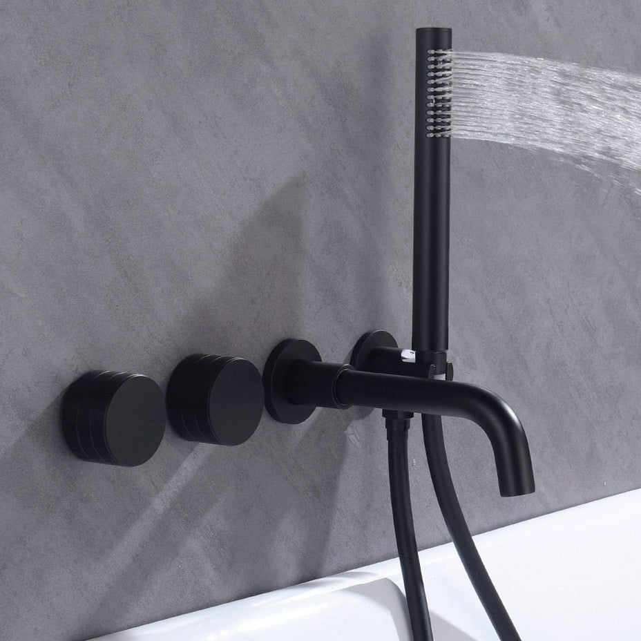 A modern AllFixture Bathroom Shower Faucet Set Mixer Valve with Bathtub Filler, featuring a black matte finish, is mounted on a grey tiled wall. The setup includes two round knobs and a sleek hand-held showerhead, which is spraying water. The system, combining both the shower and bathroom sink faucets, is positioned above a white bathtub.