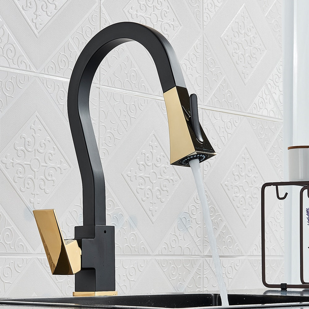 A modern kitchen features the Rozin Gourmet Kitchen Faucet with Flexible Pull Down Sprayer, elegantly designed in black and gold, set against a white textured tile backsplash. Water cascades from the faucet into a sleek dark countertop sink. In the background, a small wire shelf adorned with a lavender sprig and soap dispenser adds to the contemporary appeal of the space.