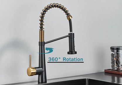 A modern Rozin Deck Mounted Pull Down Sprayer Kitchen Sink Faucet, featuring a sleek black finish with gold accents, is installed over a stainless steel sink. The faucet boasts a curved, flexible spring spout with a convenient pull-down sprayer. In the background, jars and a white panel on the wall enhance the sleek design.