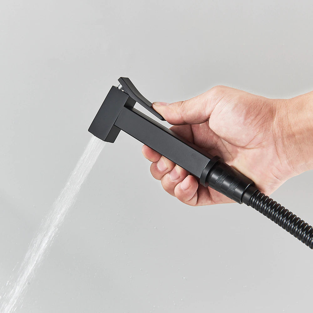 A modern black Wall Mounted Toilet Sprayer Bidet Faucet by Morsale.com, mounted on a light grey wall beside the bathroom sink faucet. This matte black set features a handheld sprayer with a top button and a flexible hose connected to a square wall bracket with a lever handle. The design is sleek, characterized by its smooth and angular lines.