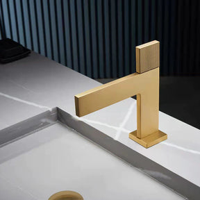 A sleek, modern Mike Jake Single Handle Brass Bathroom Sink Faucet in gold is pouring water into a gray sink. The sink, reminiscent of high-end bathroom fixtures, features a minimalist design with clean lines. The background shows vertical paneling, adding a contemporary touch to the setting.