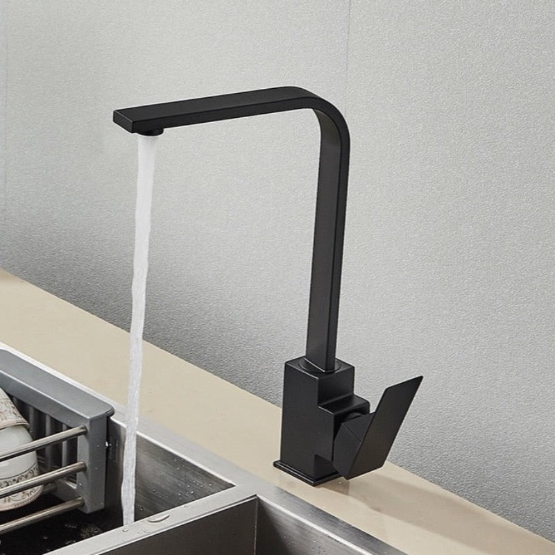 A contemporary Deck Mounted Matte Black Single Handle Kitchen Faucet by Rozin with a right-angled design is installed above the sink. Water is flowing from the faucet into the sink, with dishes stacked on a drying rack beside it. The background features a light-colored textured wall, reminiscent of sleek bathroom faucets found in modern homes.