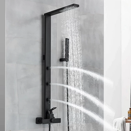 The tiled shower area features a Matte Black Wall Mounted Shower Panel With Massage Jets from Morsale.com. The panel boasts a rainfall showerhead, handheld shower wand, and three horizontal body jets, all emitting streams of water simultaneously. Complementing the sleek design are matching bathroom faucets and a white towel hanging on a nearby rack.