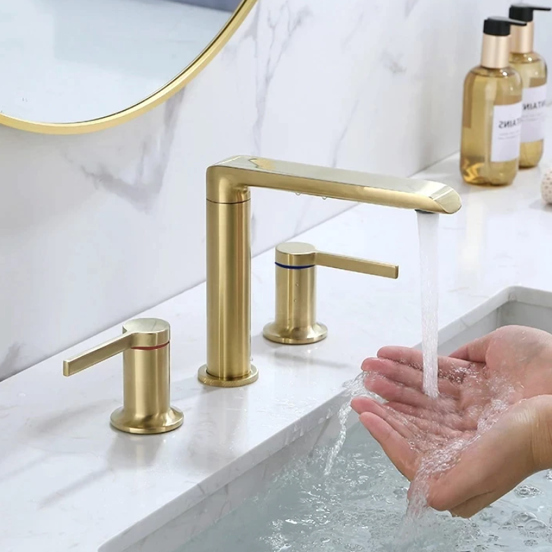 A Dual Handle Solid Brass Bathroom Sink Faucet from Morsale.com, featuring a brushed gold finish, is installed on a white marble countertop. The set includes a sleek spout and two handles—one marked with red for hot water and one with blue for cold water—perfectly complementing the elegance of the bathroom faucets collection.