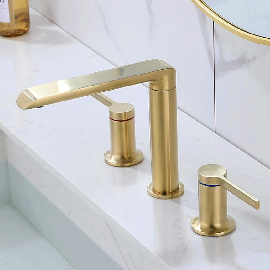 A Dual Handle Solid Brass Bathroom Sink Faucet from Morsale.com, featuring a brushed gold finish, is installed on a white marble countertop. The set includes a sleek spout and two handles—one marked with red for hot water and one with blue for cold water—perfectly complementing the elegance of the bathroom faucets collection.