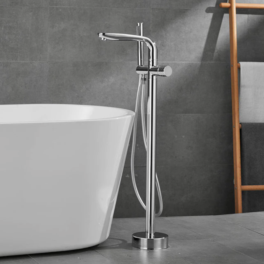 A modern bathroom features the Solid Brass Floor Bathtub Faucet Shower Mixer by Mike Jake, its gold tones pouring water into a freestanding white bathtub. The background is composed of gray tiles, and a wooden ladder shelf holding towels is partially visible. Adjacent to the setup, a sleek bathroom sink faucet enhances the contemporary design.