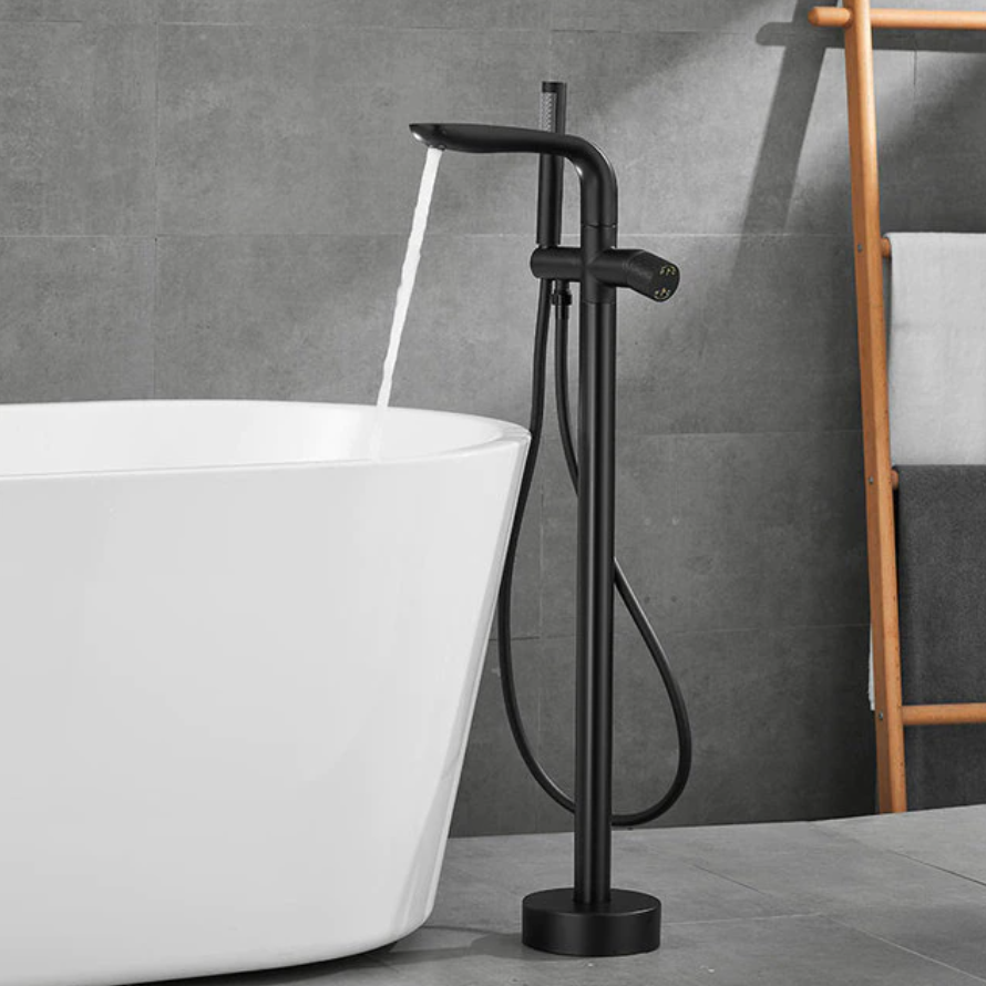 A modern bathroom features the Solid Brass Floor Bathtub Faucet Shower Mixer by Mike Jake, its gold tones pouring water into a freestanding white bathtub. The background is composed of gray tiles, and a wooden ladder shelf holding towels is partially visible. Adjacent to the setup, a sleek bathroom sink faucet enhances the contemporary design.