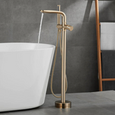 A modern bathroom features the Solid Brass Floor Bathtub Faucet Shower Mixer by Mike Jake, its gold tones pouring water into a freestanding white bathtub. The background is composed of gray tiles, and a wooden ladder shelf holding towels is partially visible. Adjacent to the setup, a sleek bathroom sink faucet enhances the contemporary design.