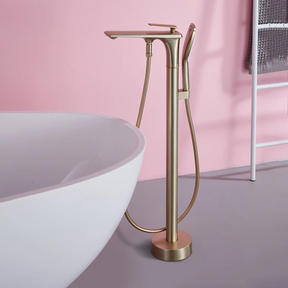 A modern bathroom featuring a freestanding bathtub complemented by a Mike Jake Brushed Gold Floor Mounted Bathtub Faucet Shower Mixer. The wall behind the tub is elegantly adorned with white marble, while a white towel drapes over the edge of the tub. To the right, a wooden door frame peeks into view.