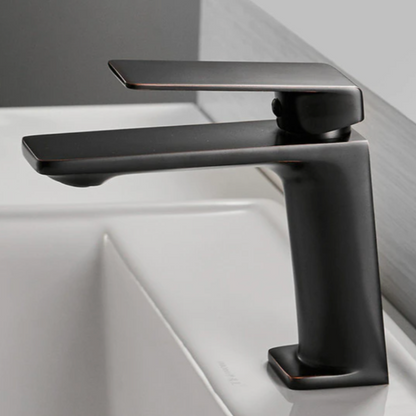 A sleek, modern Wanfan Single Handle Bathroom Sink Faucet in black, featuring clean lines and an angular design, is mounted on a white sink in the bathroom. The single lever handle is positioned over the base, creating a minimalist and contemporary look against a light grey background.