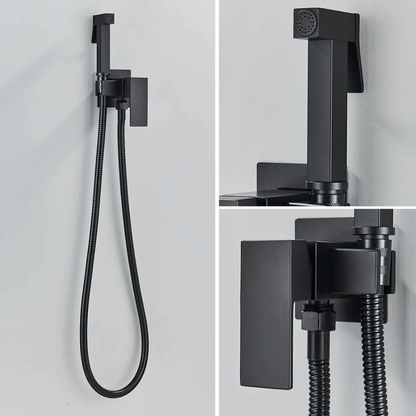 A modern black Wall Mounted Toilet Sprayer Bidet Faucet by Morsale.com, mounted on a light grey wall beside the bathroom sink faucet. This matte black set features a handheld sprayer with a top button and a flexible hose connected to a square wall bracket with a lever handle. The design is sleek, characterized by its smooth and angular lines.