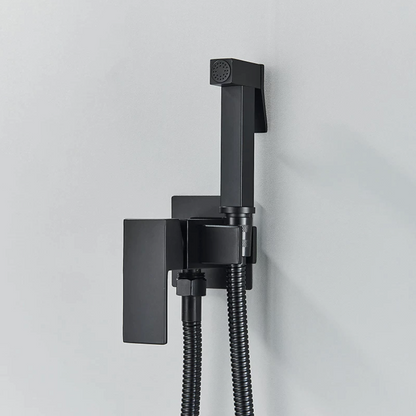 A modern black Wall Mounted Toilet Sprayer Bidet Faucet by Morsale.com, mounted on a light grey wall beside the bathroom sink faucet. This matte black set features a handheld sprayer with a top button and a flexible hose connected to a square wall bracket with a lever handle. The design is sleek, characterized by its smooth and angular lines.