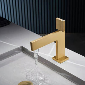 A sleek, modern Mike Jake Single Handle Brass Bathroom Sink Faucet in gold is pouring water into a gray sink. The sink, reminiscent of high-end bathroom fixtures, features a minimalist design with clean lines. The background shows vertical paneling, adding a contemporary touch to the setting.