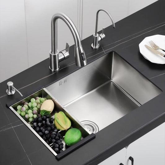 The AllFixture 304 Stainless Steel Single Bowl Undermount Kitchen Sink, with its sleek, modern design and stainless steel finish, includes a cutting board insert holding an assortment of fruits and vegetables such as grapes, an avocado, a lime, and an apple. Paired with a stylish kitchen sink faucet, the sink is elegantly set in a dark countertop with a plate and cutlery nearby.