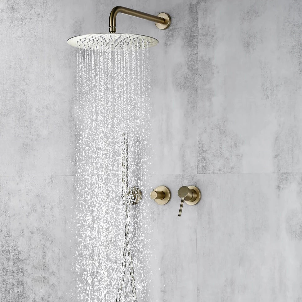 A modern minimalist shower setup features the Wasser™ Brushed Gold Shower System with Handheld Sprayer by Morsale.com, showcasing a large, round, wall-mounted rain showerhead and a sleek handheld shower spray emitting water. The brushed gold fixtures, including complementary bathroom faucets, accentuate the textured gray tile wall. Two control knobs are visible below.