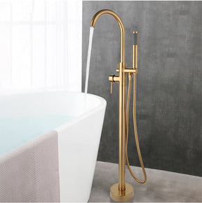 A modern bathroom featuring a sleek, golden Wasser™ Floor Mounted Bathtub Filler Shower System from Morsale.com with water flowing into a white bathtub. The background showcases a gray textured wall and a partially visible white curtain on the left side. A beige towel hangs over the edge of the tub, complementing the elegant bathroom faucets.