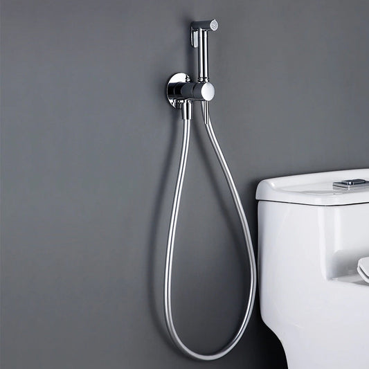 A modern bathroom with a gray wall features the allfixture Wall-Mounted Brass Bidet Faucet attached next to a white toilet. The bidet handle is mounted on a circular bracket, with a flexible hose extending downwards. Nearby, matching bathroom faucets add to the contemporary aesthetic.