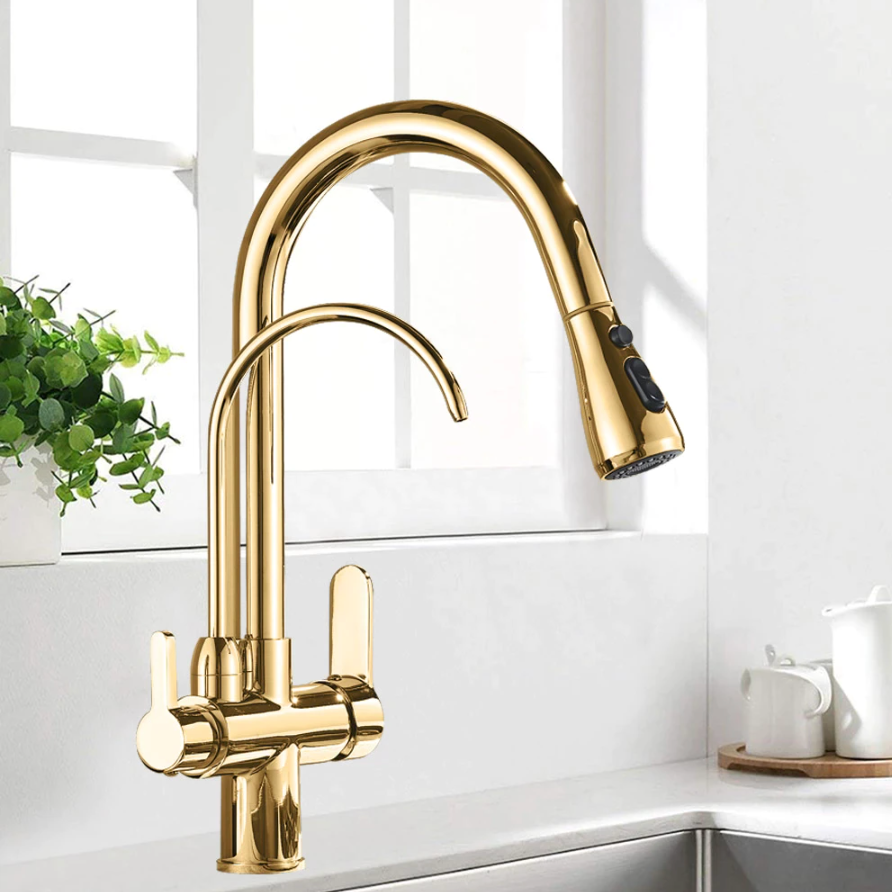 A modern Rozin Solid Brass Kitchen Faucet with Pull Out Sprayer & Filtered Water Tap in a polished gold finish is mounted on a white countertop beneath a window. The faucet features a high arc and dual handles. A small plant is visible on the windowsill, and a white kettle and mug are situated in the background.